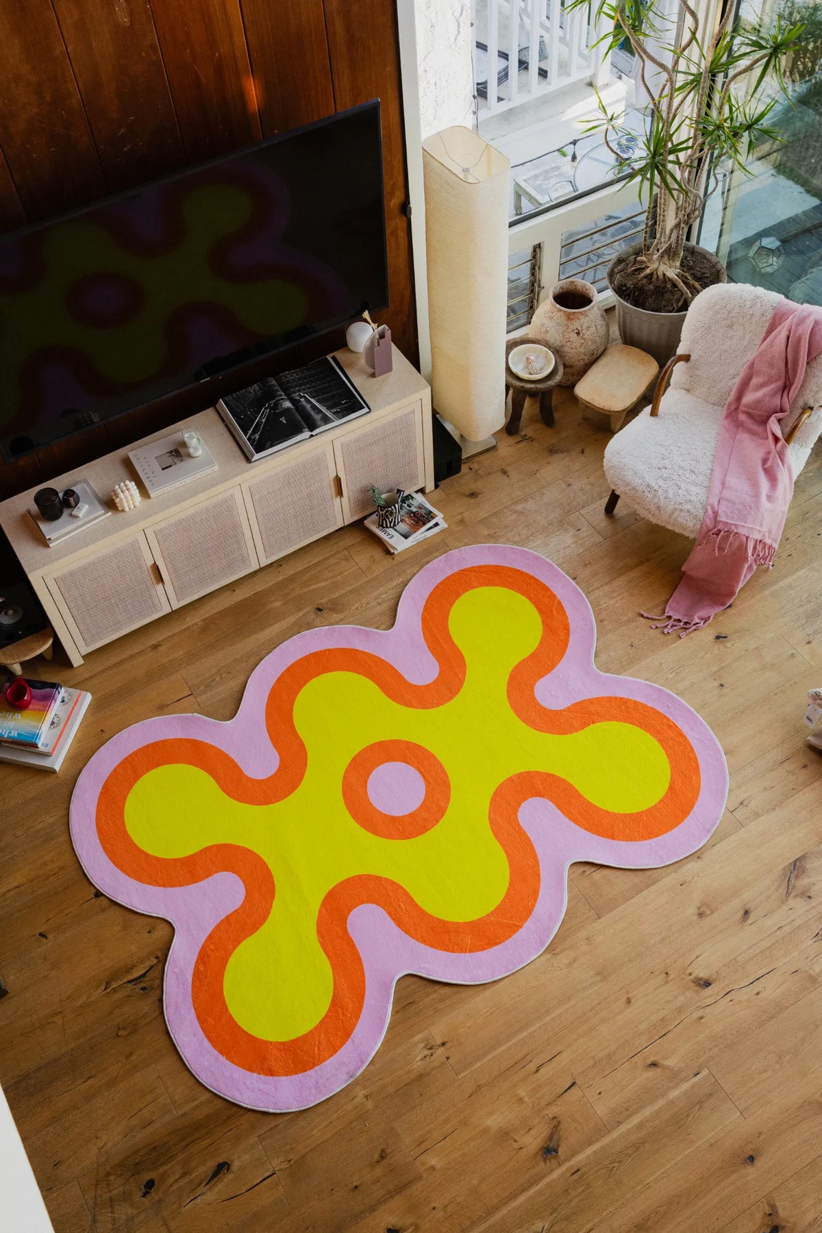 Yellow rug with orange and pink outlines laid out in front of a TV console and armchair by large windows.