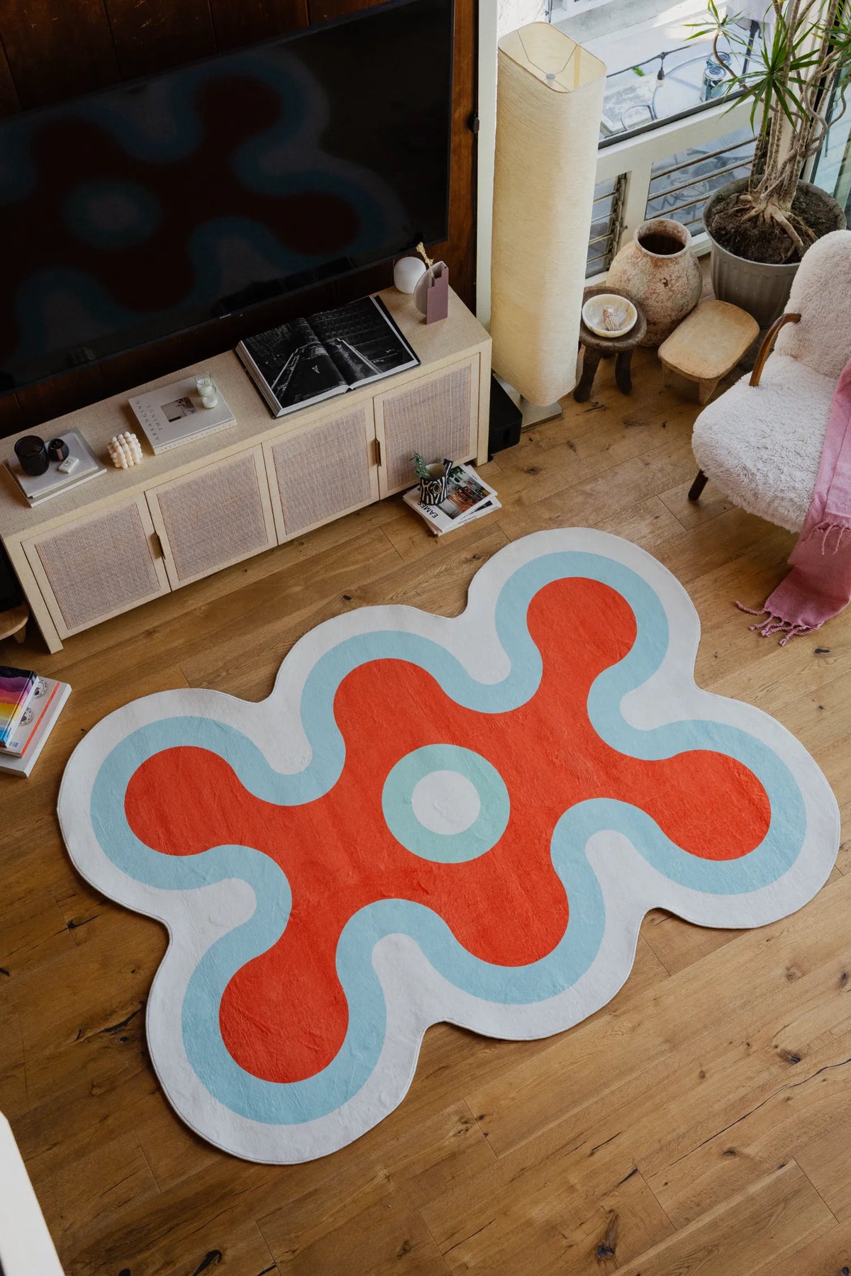 Top view of the red, white, and blue coral rug in a cozy corner, surrounded by books, TV console, and soft seating.