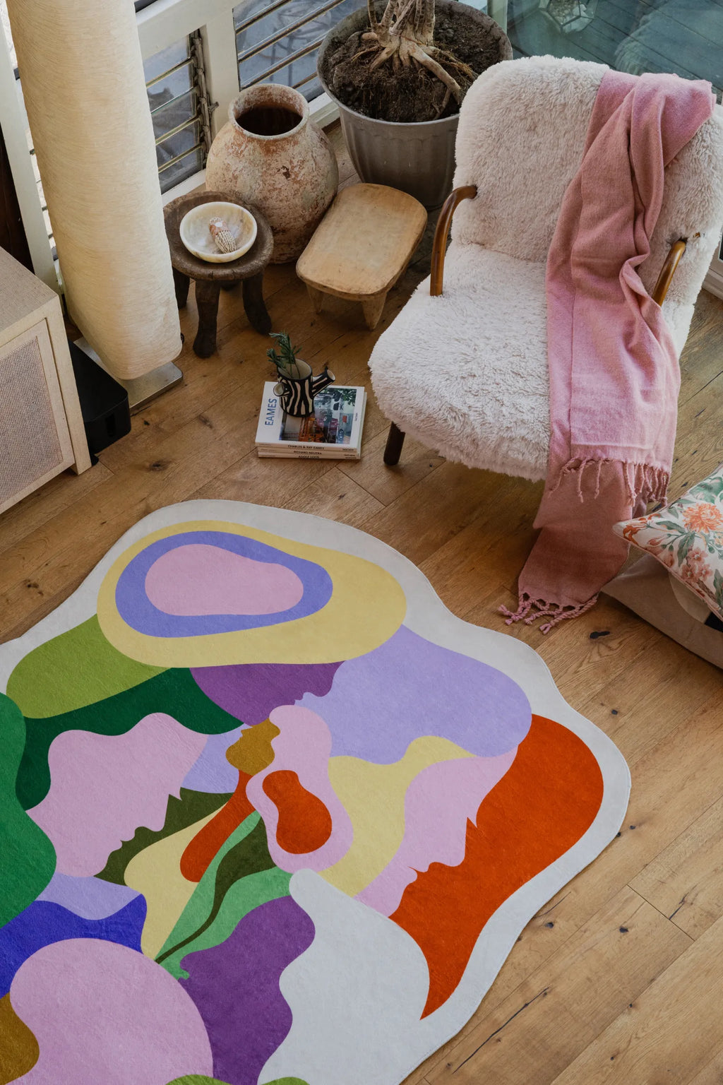Close-up of the Bloomland Unity pastel rug’s upper corner, highlighting its curvy silhouette and colorful abstract shapes near a boucle chair draped with a pink scarf.
