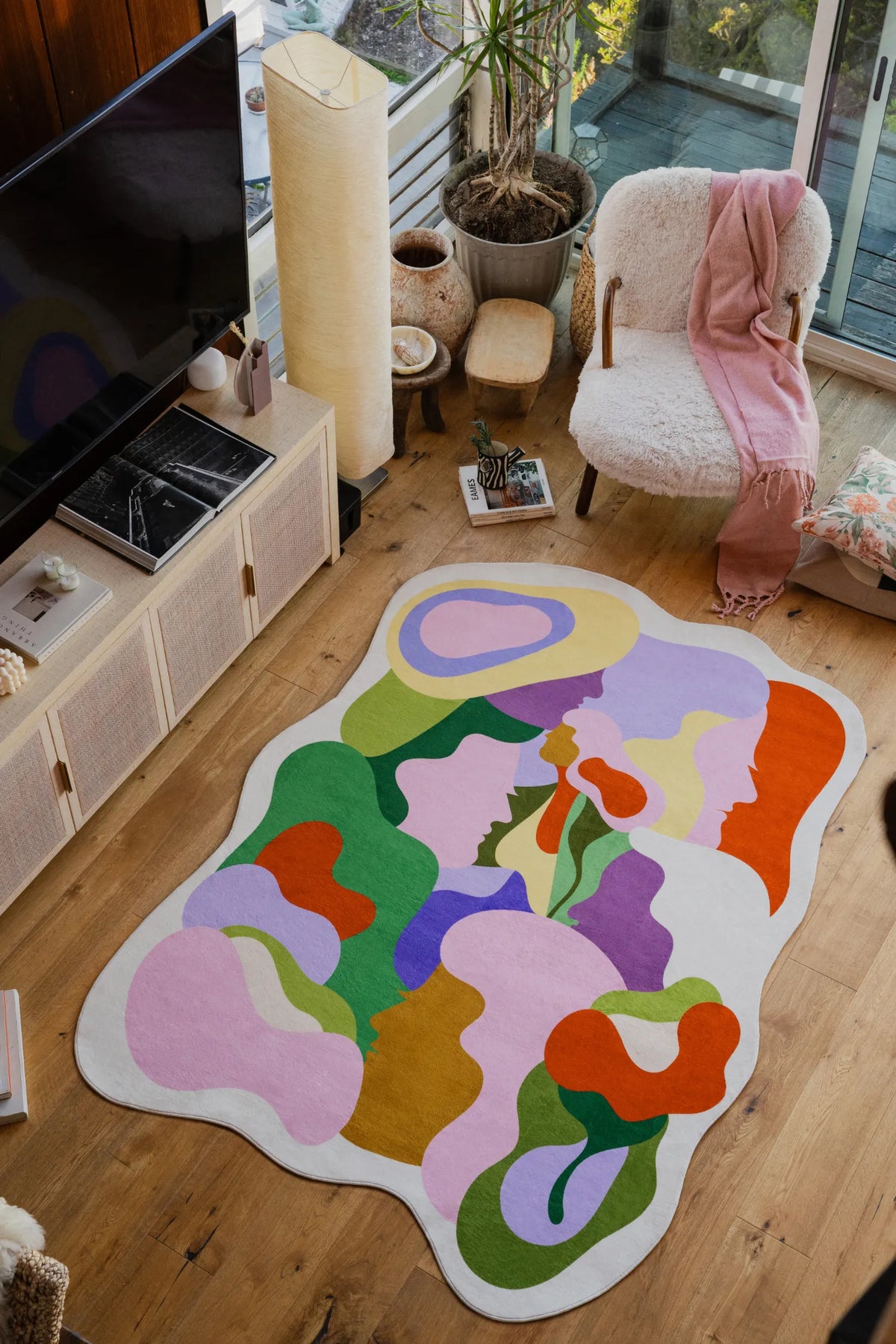 Irregular Bloomland Unity Pastel Rug placed in a cozy living room with a boucle armchair, pink scarf, and floral cushion by the window.