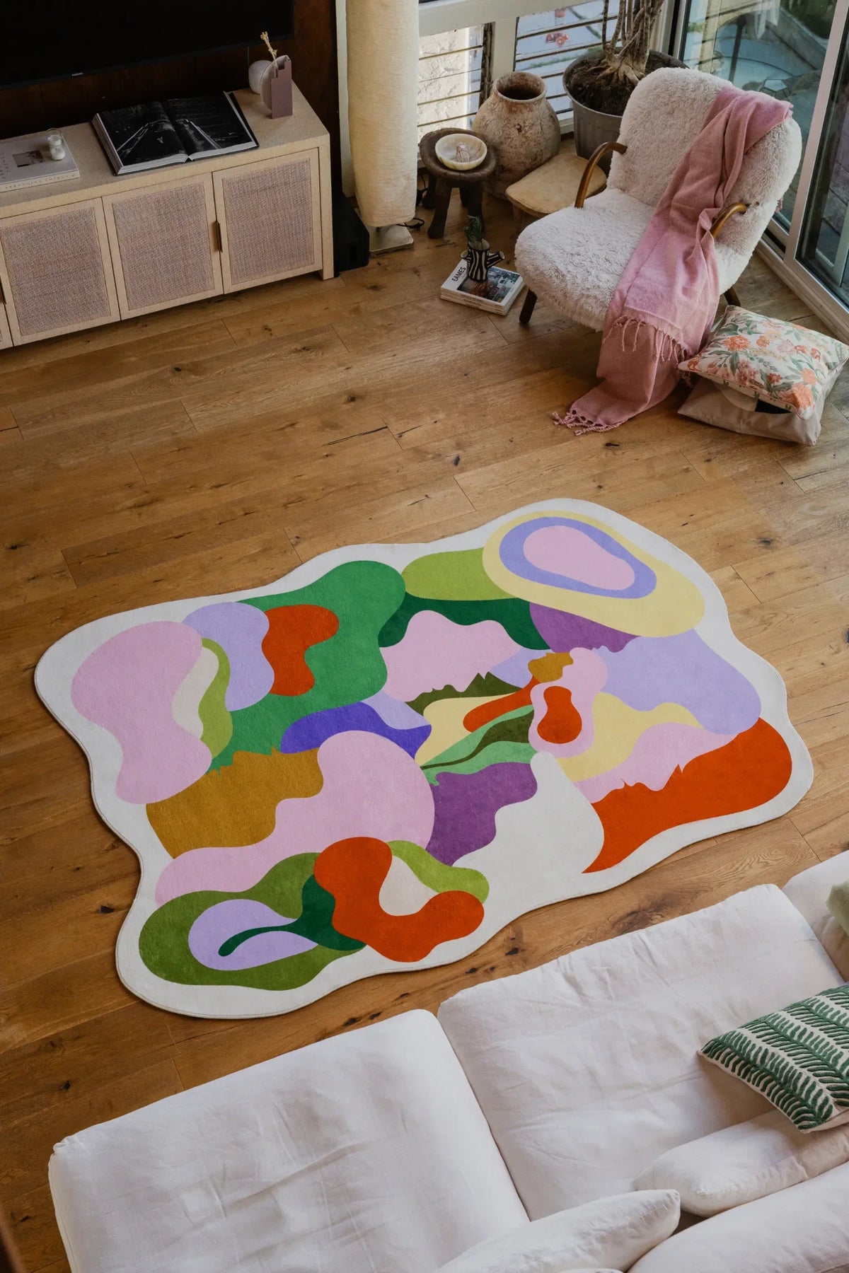 Top view of the Bloomland Unity pastel rug beside a white sofa and boucle chair in a bright living room.