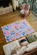 Lavender Base Purple Floral Wavy Rug by Jessica Miller placed on light wood flooring beside a cream sofa.