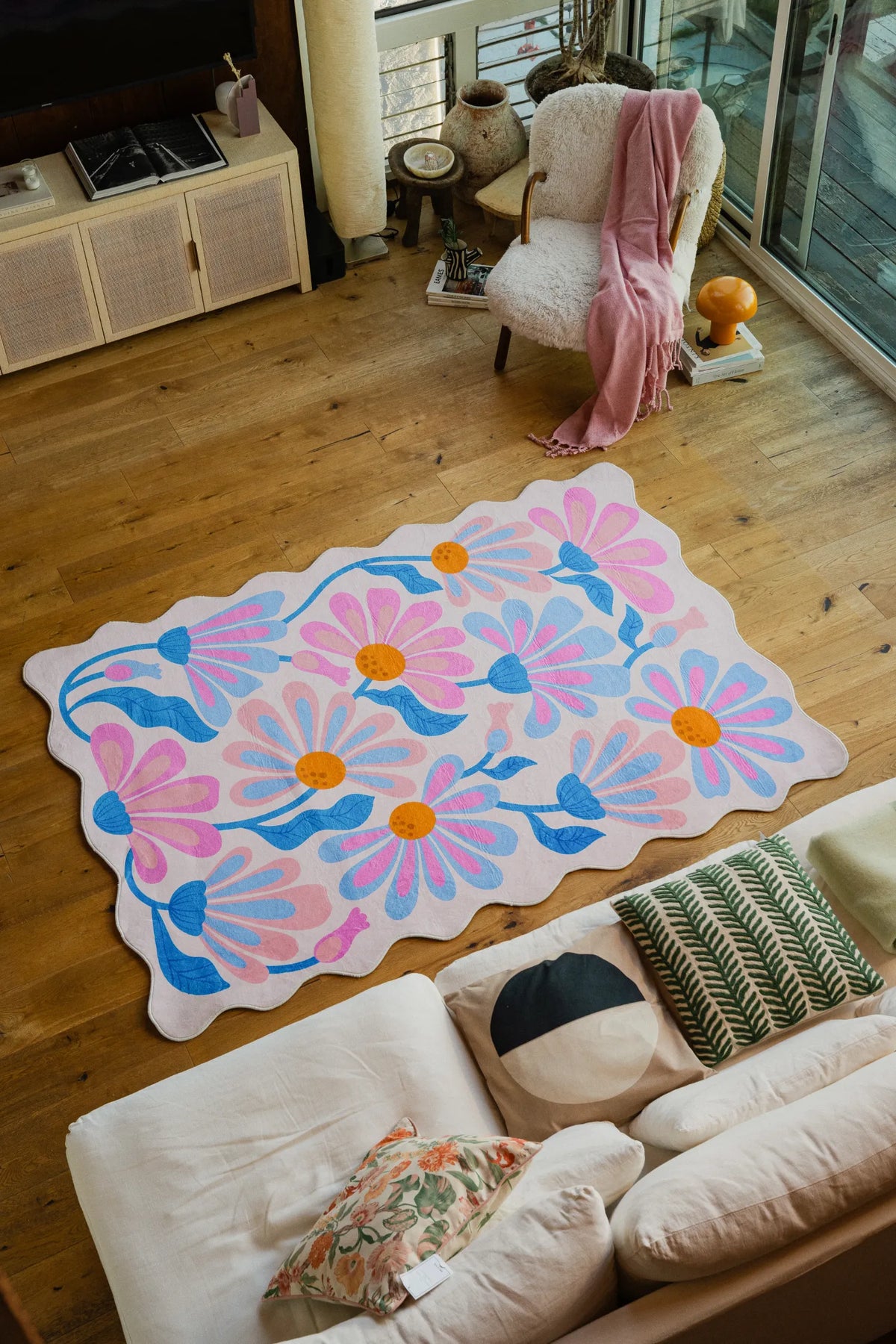 Lavender Base Purple Floral Wavy Rug by Jessica Miller placed on light wood flooring beside a cream sofa.