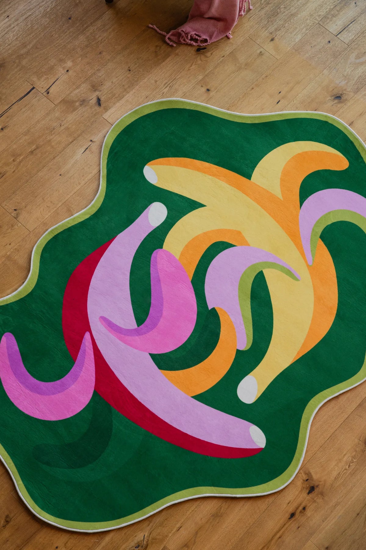 Top view of the funky bananas rug with vibrant pink and yellow curves, placed on wooden floor in a cozy corner.