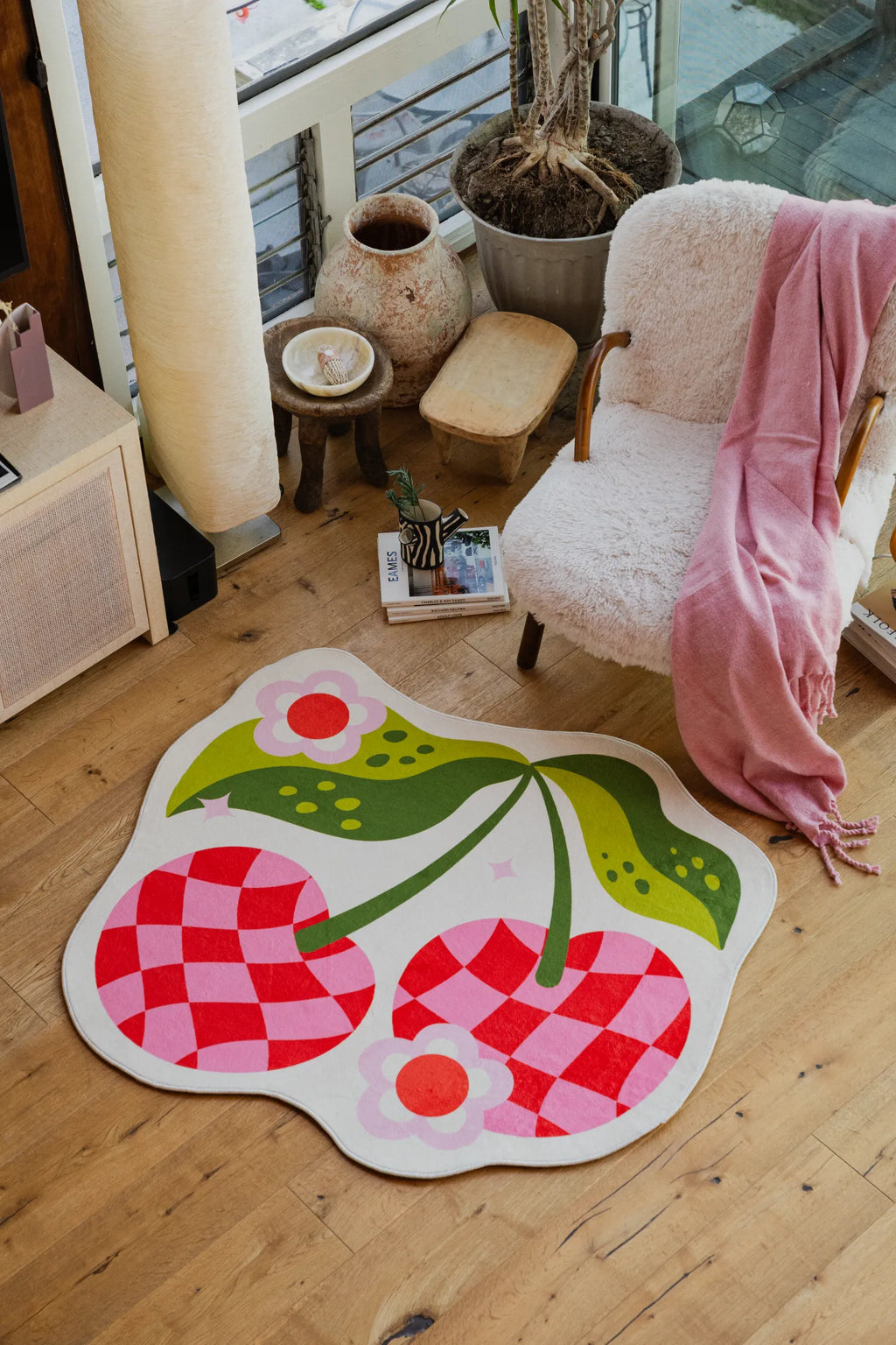 The Irregular Pink and Red Checkered Cherry Rug by Jessica Miller, 4' × 4', is placed in a cozy corner with wood floor.