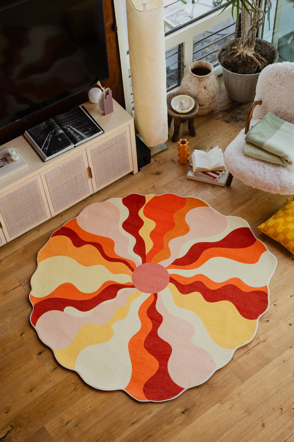 Sundial orange rug with wavy sunburst design placed by a cozy white chair and book in a bright living room corner.