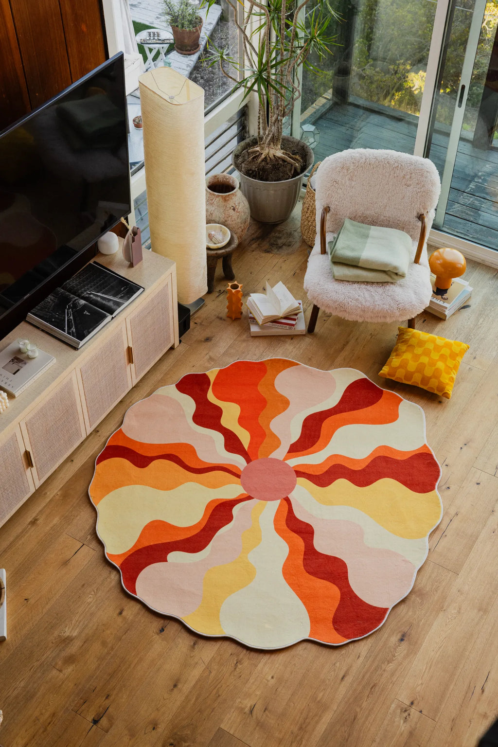 Orange sun-shaped rug in vibrant hues centered in a window-lit room with soft seating and wooden floor.