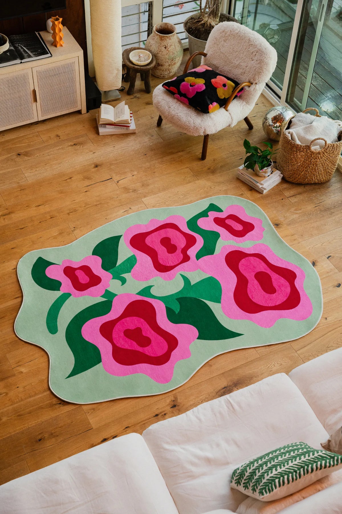 Irregular Rose Garden Floral Rug by Maggie Stephenson placed near a fuzzy chair and window wall on light wood floor.