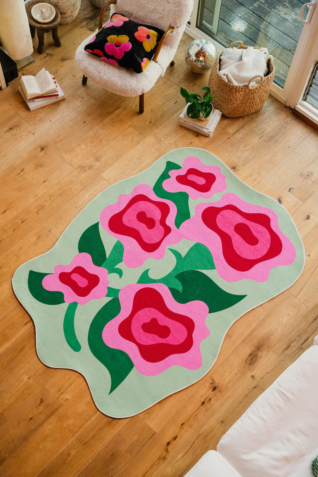 Floral rug with oversized pink roses placed in a bright living room corner beside a fuzzy chair and window.