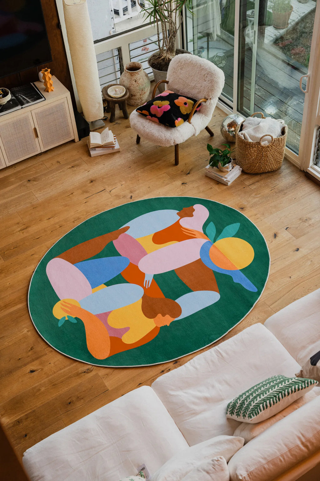 Oval Fruitvine Green Rug styled in a cozy living room with a white boucle chair, floral cushion, and woven storage basket