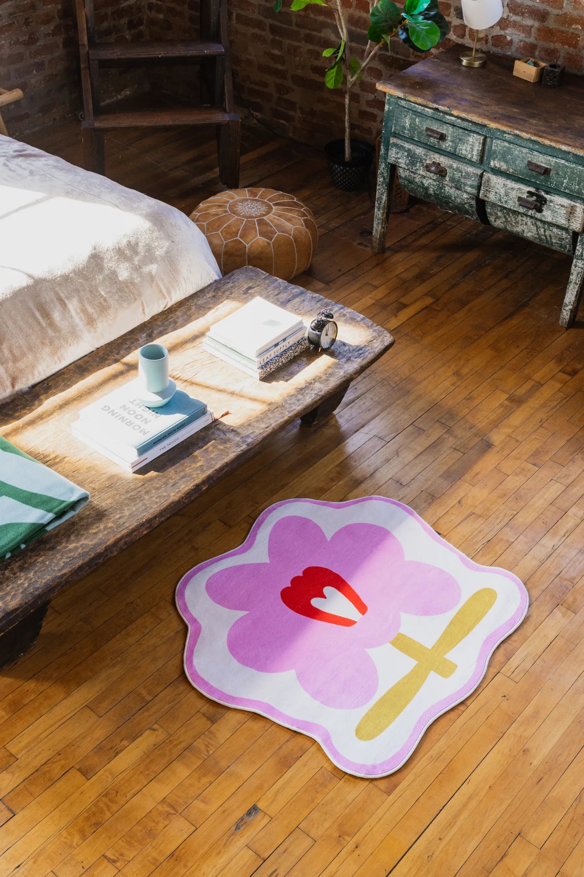 Flower Rug by Anne Julie in pink version placed neatly beside rustic wood rustic bench on polished floor.