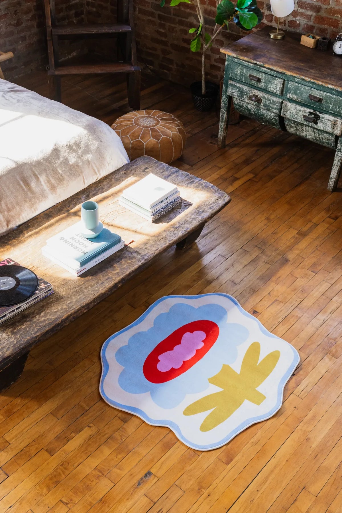 Blue flower rug with bold red center brightening wood floor beside vintage table and natural light.
