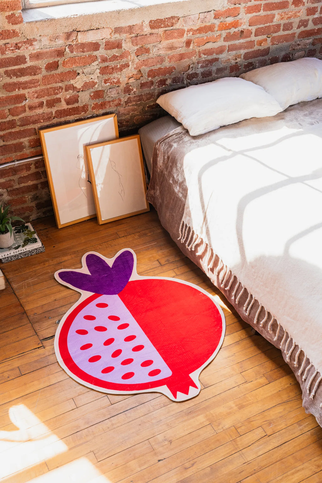 Red Pomegranate Shaped Irregular Rug by Shayla Goethe placed beside a bed in a loft room, sunlight casting shadows across the wooden floor.