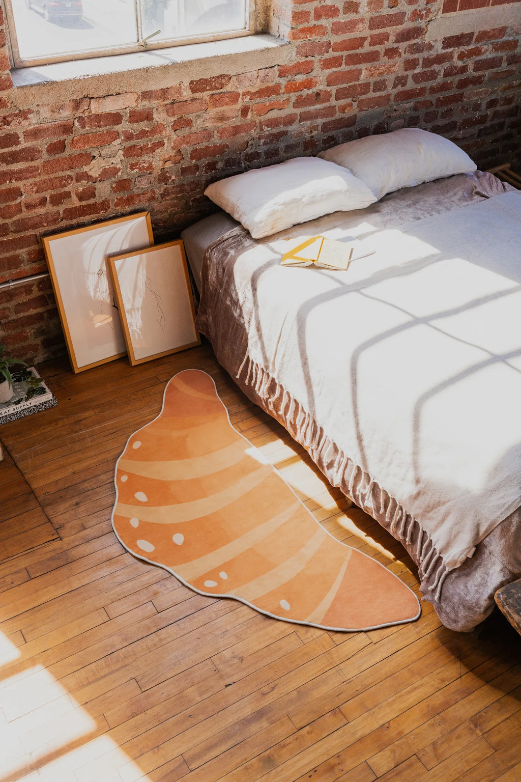Buttery Orange Croissant Rug by Petra Lizde placed beside a bed on a wooden floor with sunlight streaming in