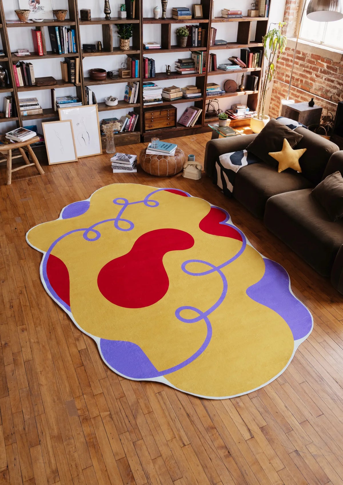 Wavy Abstract Irregular Area Rug in bright yellow with bold red and purple accents, styled in a cozy living room with a bookshelf, dark sofa and playful star cushion.