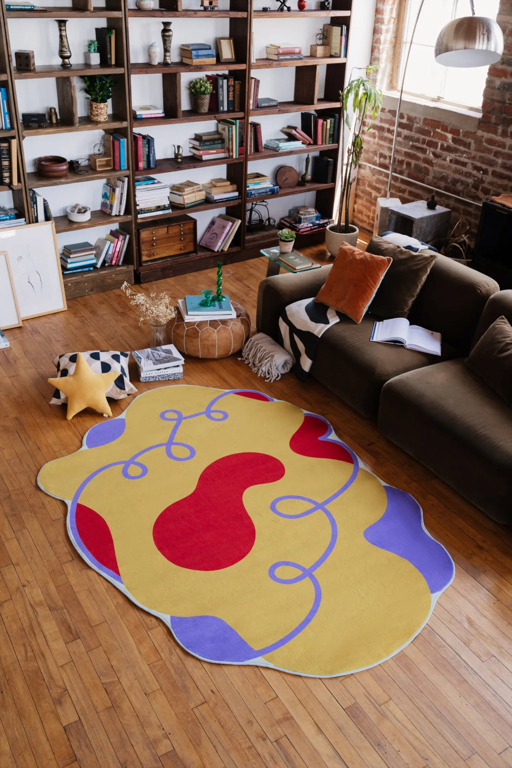 A funky wavy abstract rug in yellow with red and purple shapes, adding a vibrant pop of color to a loft-style living room with wooden floors and a comfy sofa.