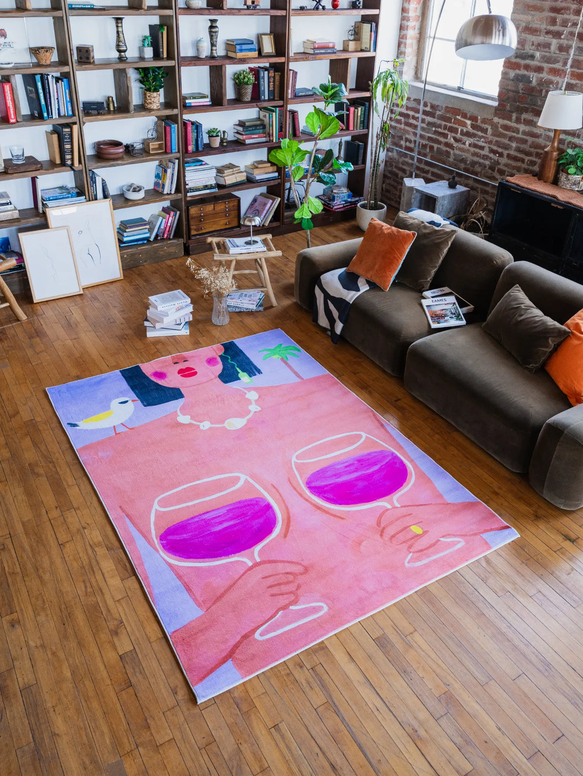 Funky Wine and Woman Art Rug by Nimei in 5'X7' spread across wood floor beside a plush sofa and tall book-filled shelves.
