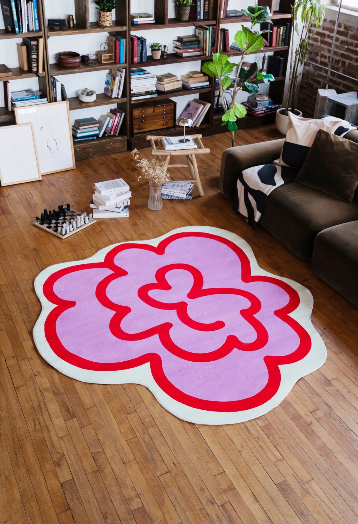 Pink funky flower shaped rug laid on wood floor in a living room beside a sofa, softening the corner with a cheerful touch.