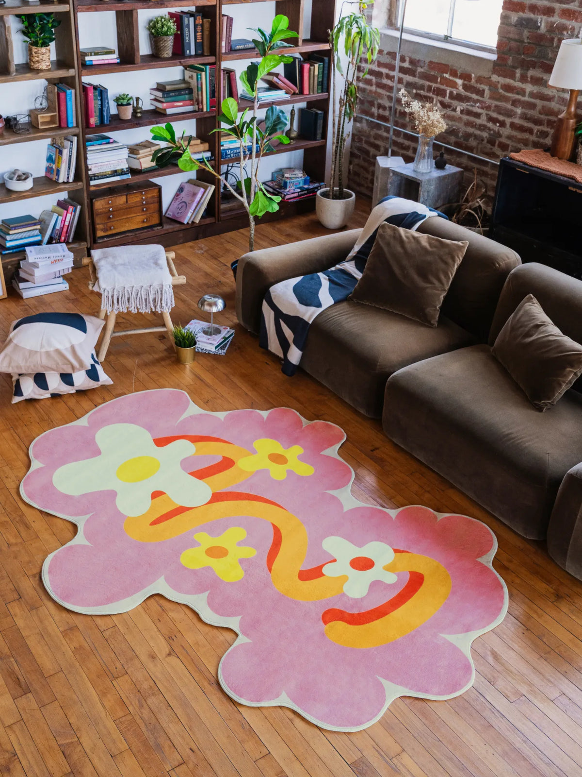 Pink Wavy Floral Shaped Irregular Rug by Shayla Goethe on wood floor in front of a deep sofa against brick wall.