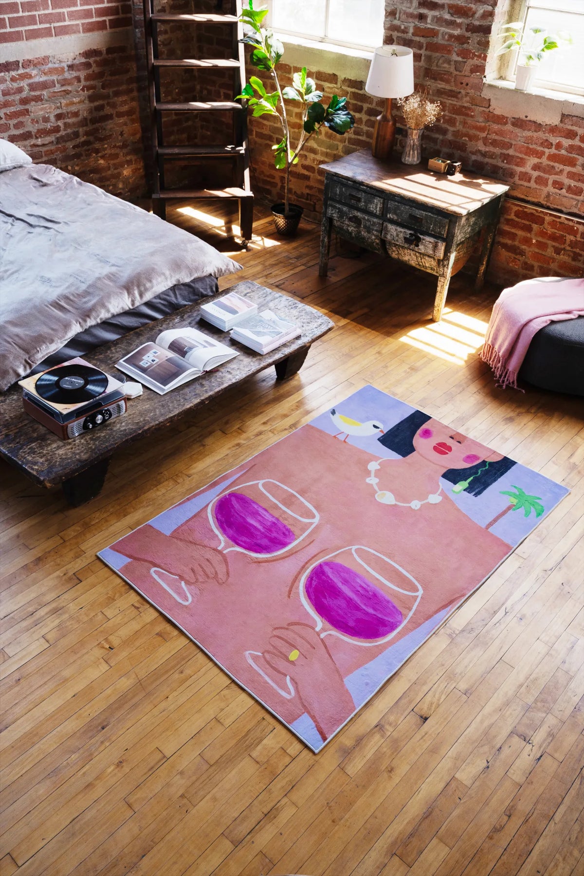 A playful rug with woman and wine design in 5'X7' resting under sunlight near rustic low table and soft draped bedding.
