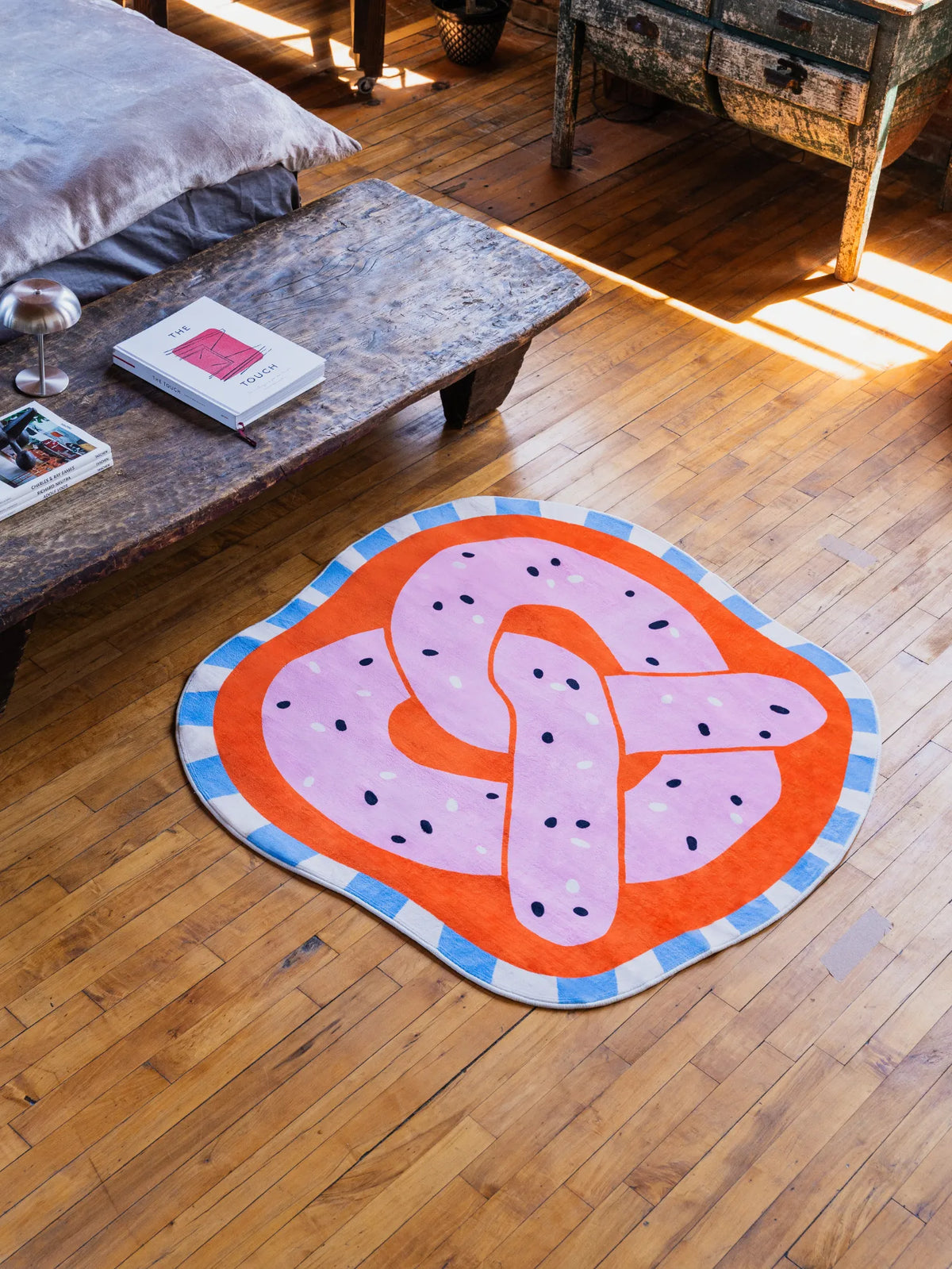 Pretzel-Shaped Cute Rug in pink styled on wood floor beside rustic long bench adding playful touch to the bedroom