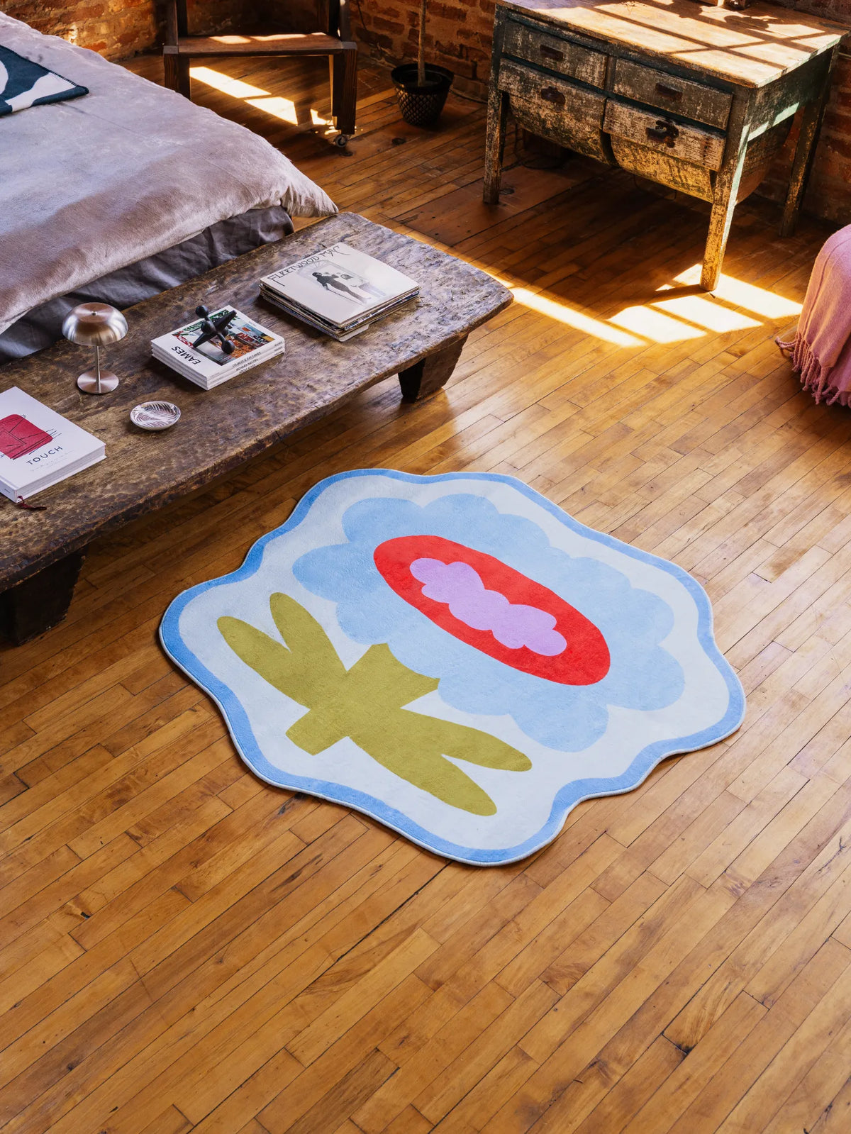 Flower Rug by Anne Julie in blue version styled neatly on wood floor beside rustic table under streaming light.