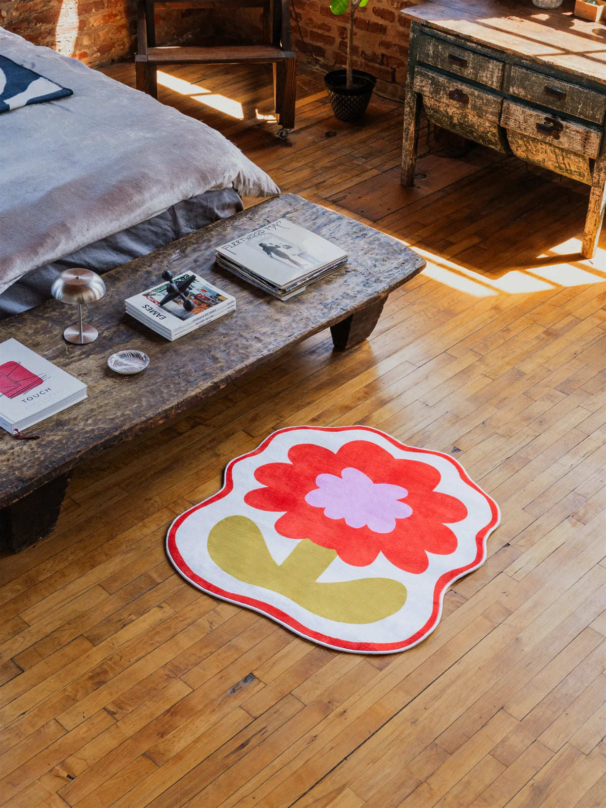 Orange flower rug bringing playful color beside coffee table stacked with books in a cozy daylight corner.