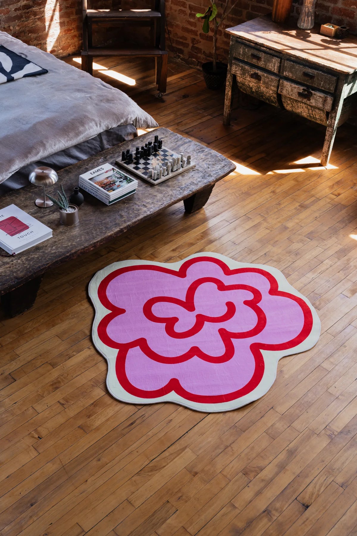 Pink Funky Flower Shaped Irregular Rug placed on wood floor in a bedroom, brightening the area beside a low stool and bed.