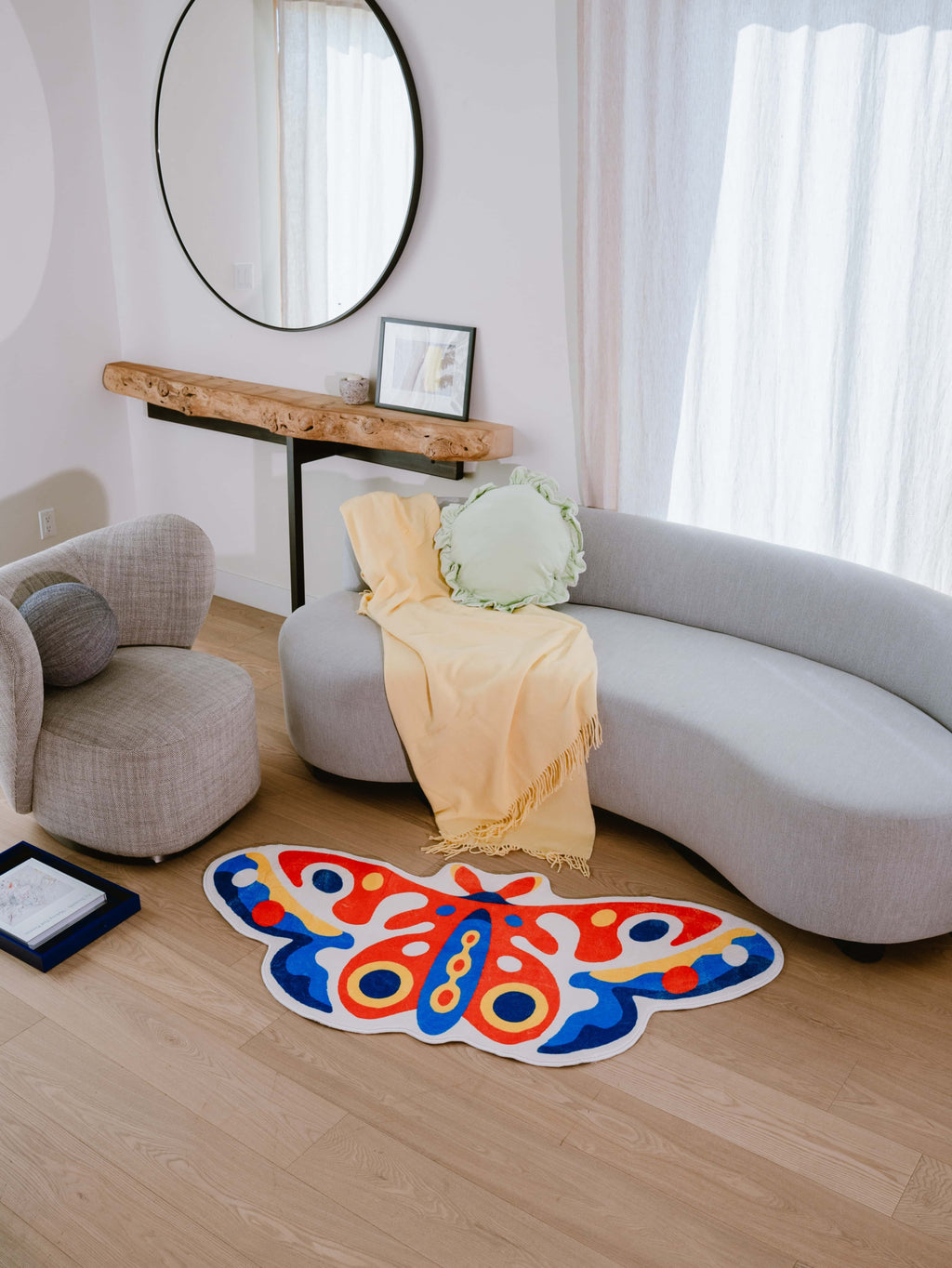 Butterfly rug on wood floor in front of a curved sofa and low console, in a softly lit neutral-toned room.