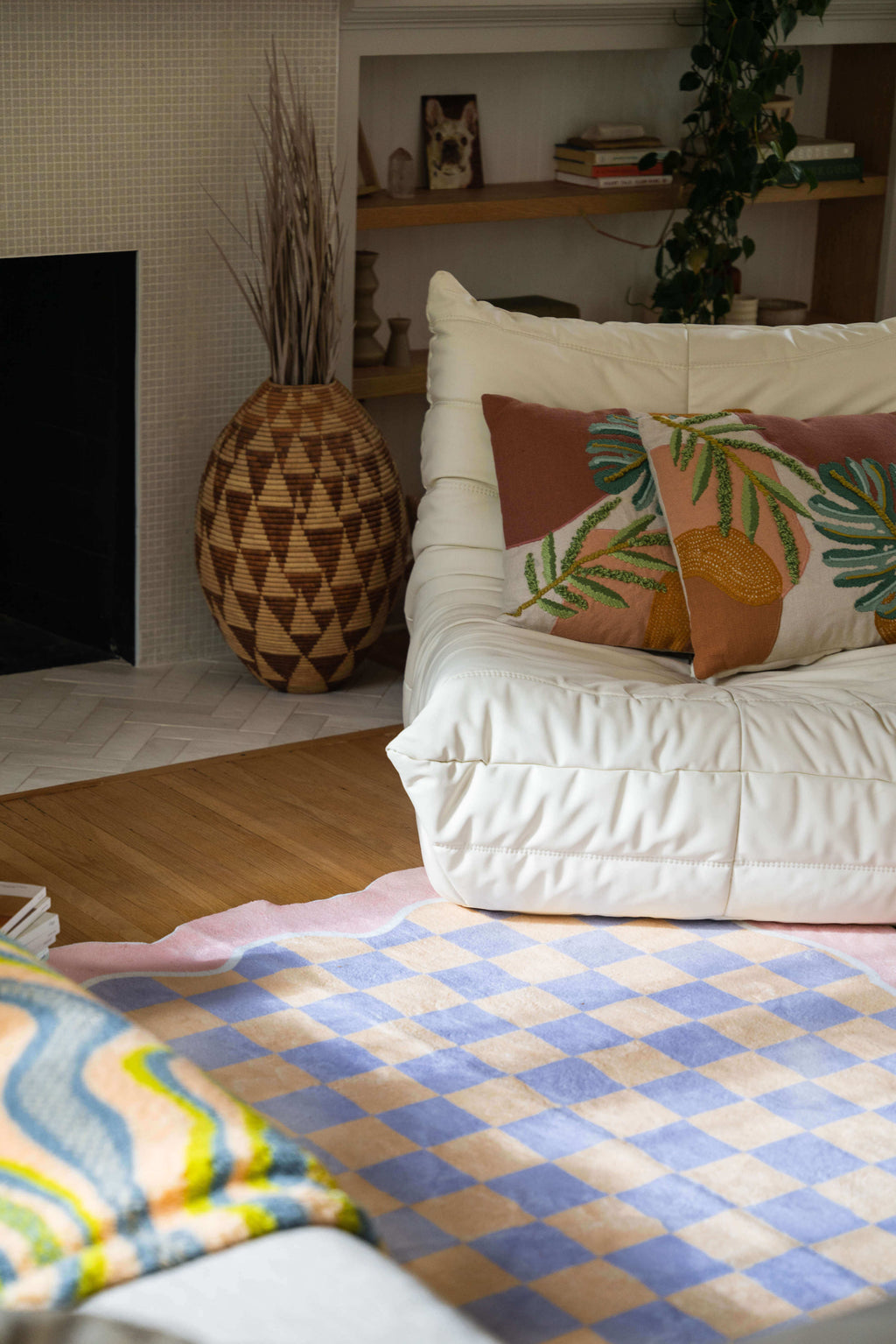 Pastel rug partially under a white lounge chair and fireplace, softly lit to highlight its peach and lavender checker pattern.