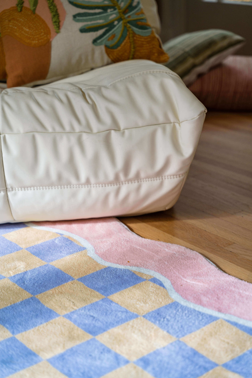 A close-up of the Mellow Pastel Rug's pink wavy border and checkered pattern next to a white lounge chair.