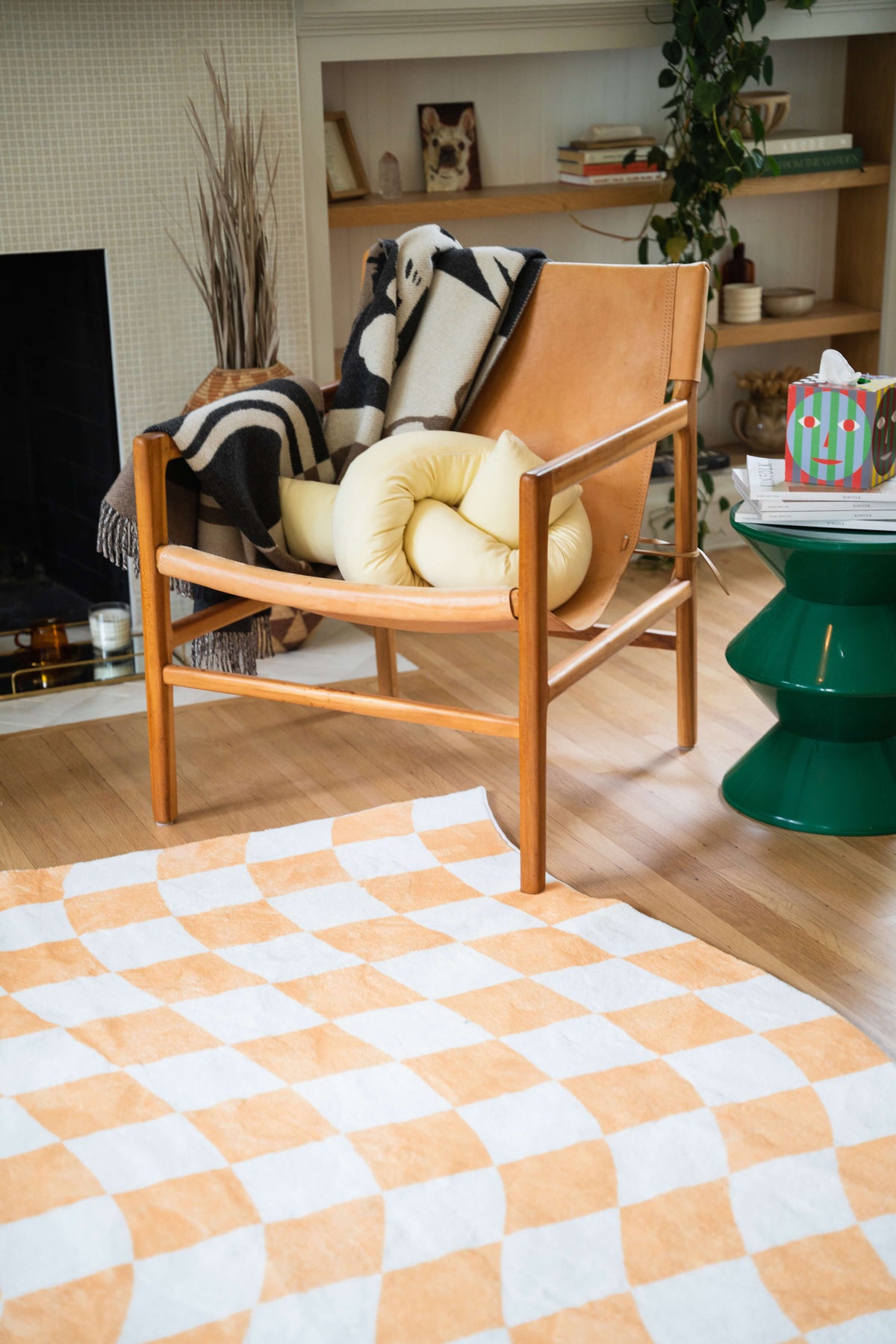 Close-up of the checkered rug under a wooden lounge chair with cozy pillows and a side table.