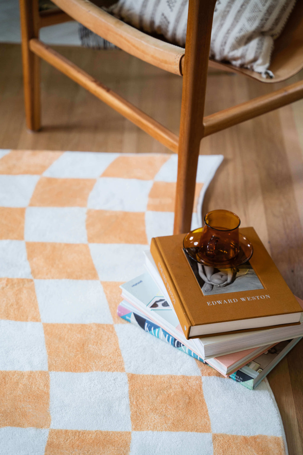 Detailed view of the Yellow Wavy Checkered Rug under a wooden chair, with books and a glass cup adding warm accents.