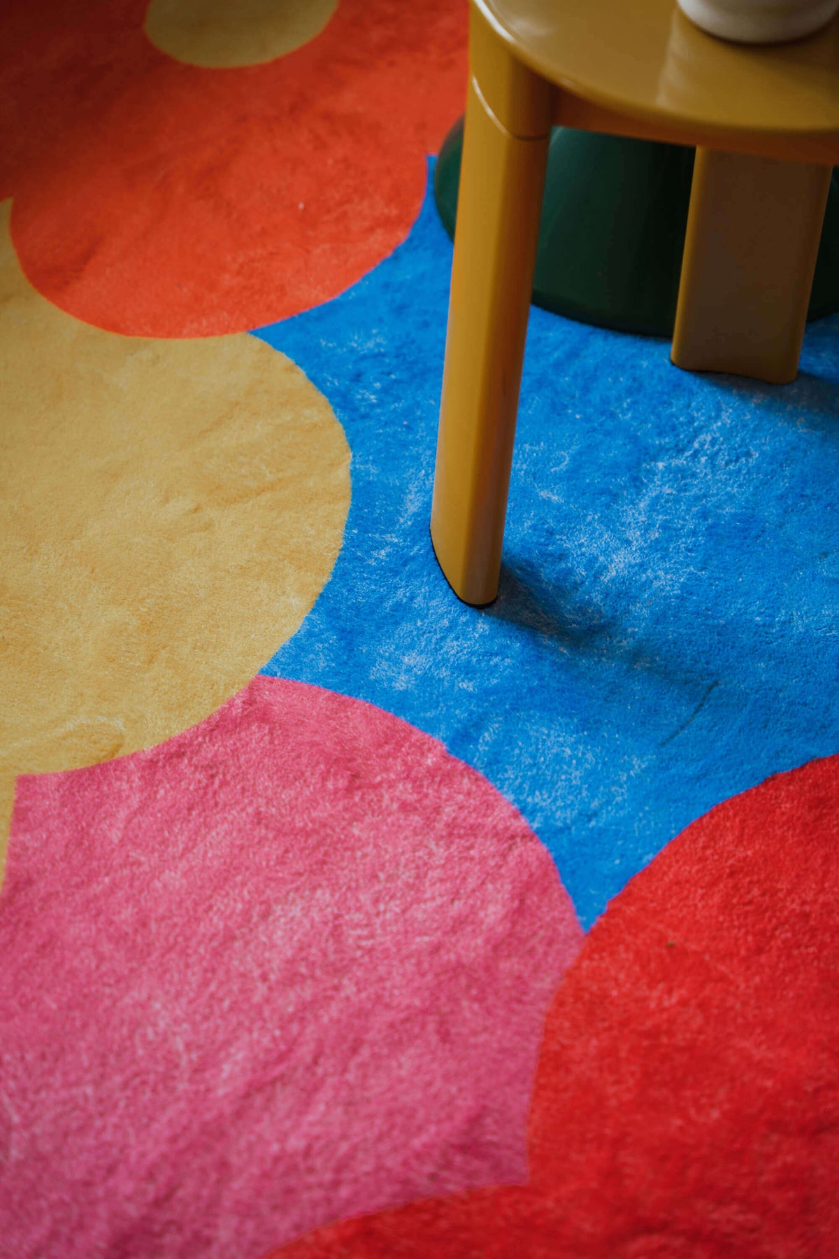 Close-up of the funky floral rug’s vivid red, yellow, pink, and blue sections beneath a mustard-yellow side table.