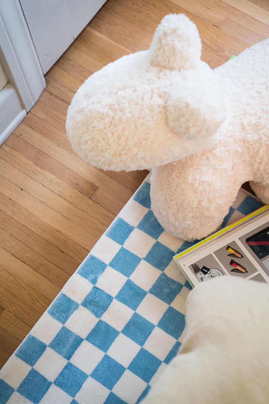 A cozy corner featuring the checkered rug, a plush white bear seat, and a stack of colorful design books.