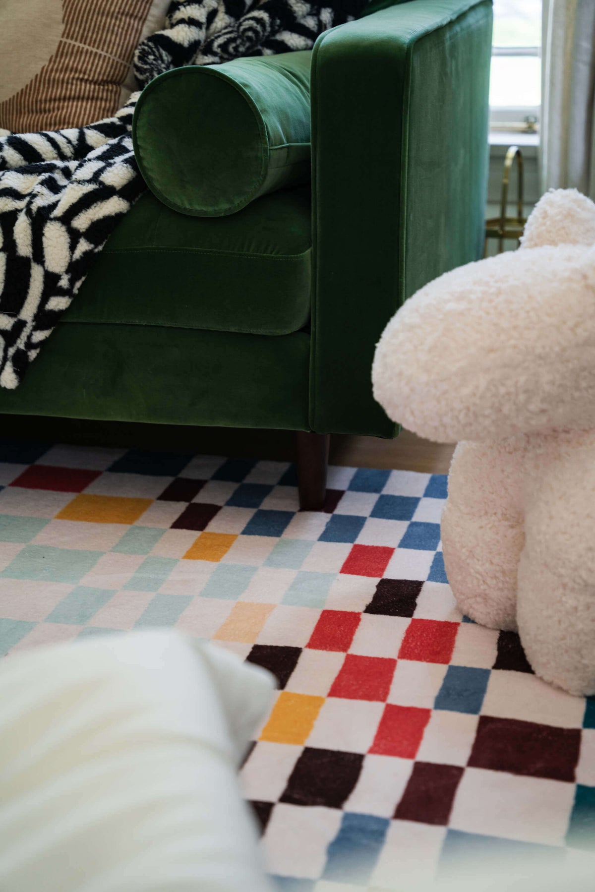 Close-up of the pixel checkered rug under a green velvet sofa and plush sculpture, showing its vivid multicolor squares.