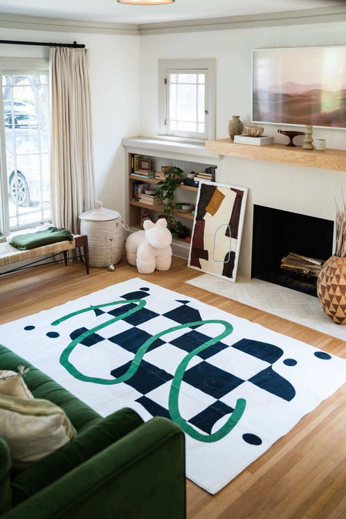 Black and White Checkered Rug in a bright living room with green sofa, fireplace, bookshelf, and plush animal decor.