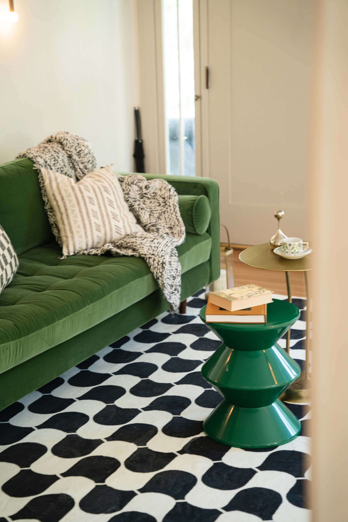 Side view of the wavy rug partially under a green velvet sofa, styled with neutral pillows and a soft throw.