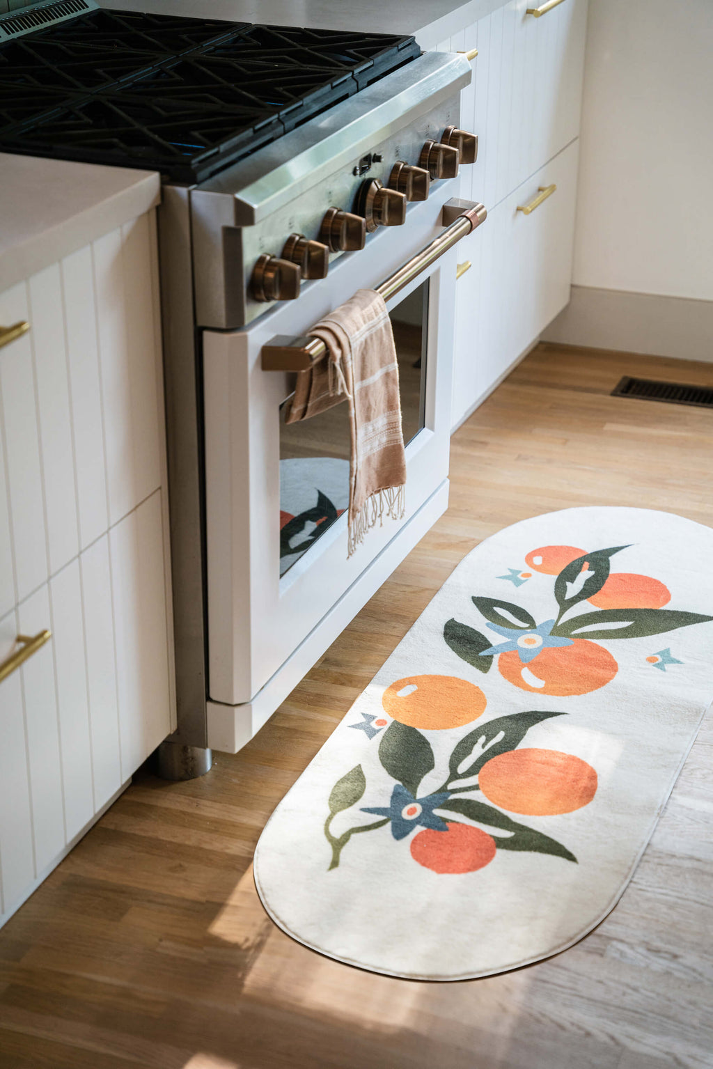 Orange Pattern Mat placed in front of a kitchen oven with white cabinetry and wooden floor.