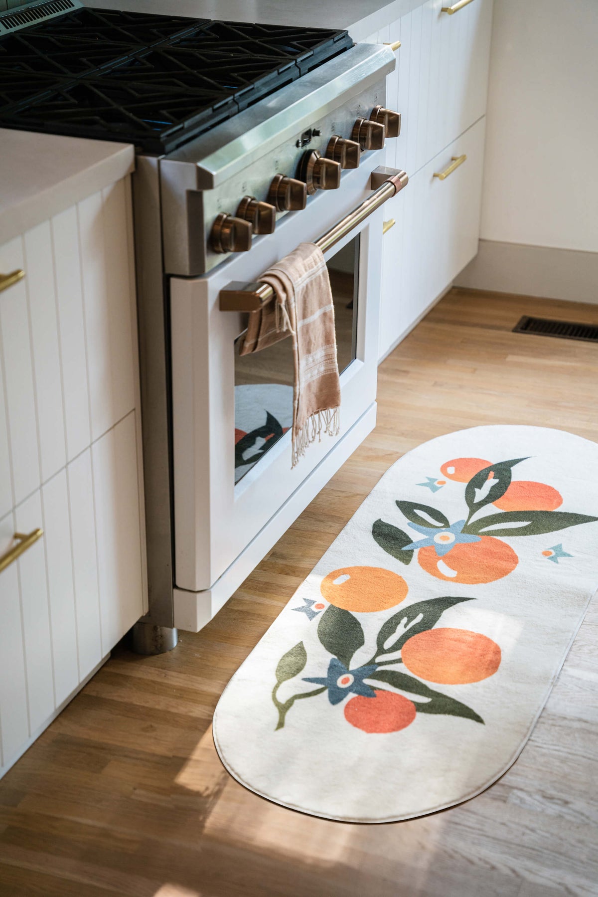 Orange Pattern Mat placed in front of a kitchen oven with white cabinetry and wooden floor.