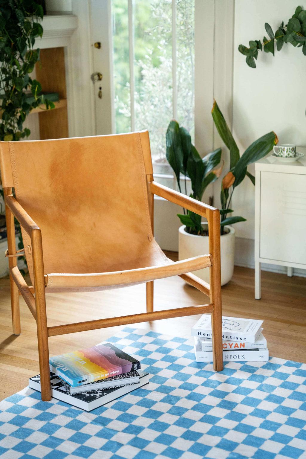 Minimal reading nook with the checkered rug beneath a leather chair, styled with art magazines and indoor plants.