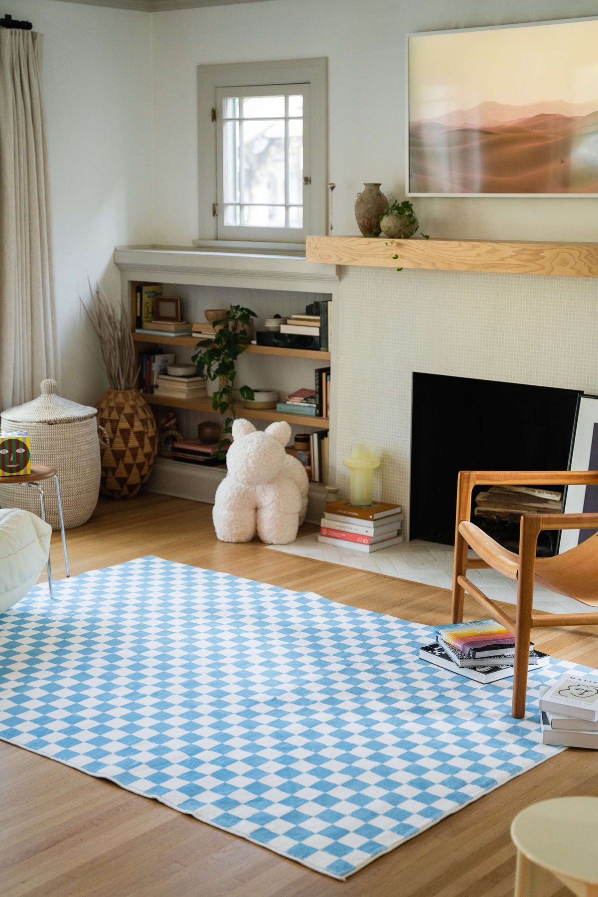 Living room with a light blue and white checkered rug placed in front of a fireplace, styled with a wooden armchair and art books.