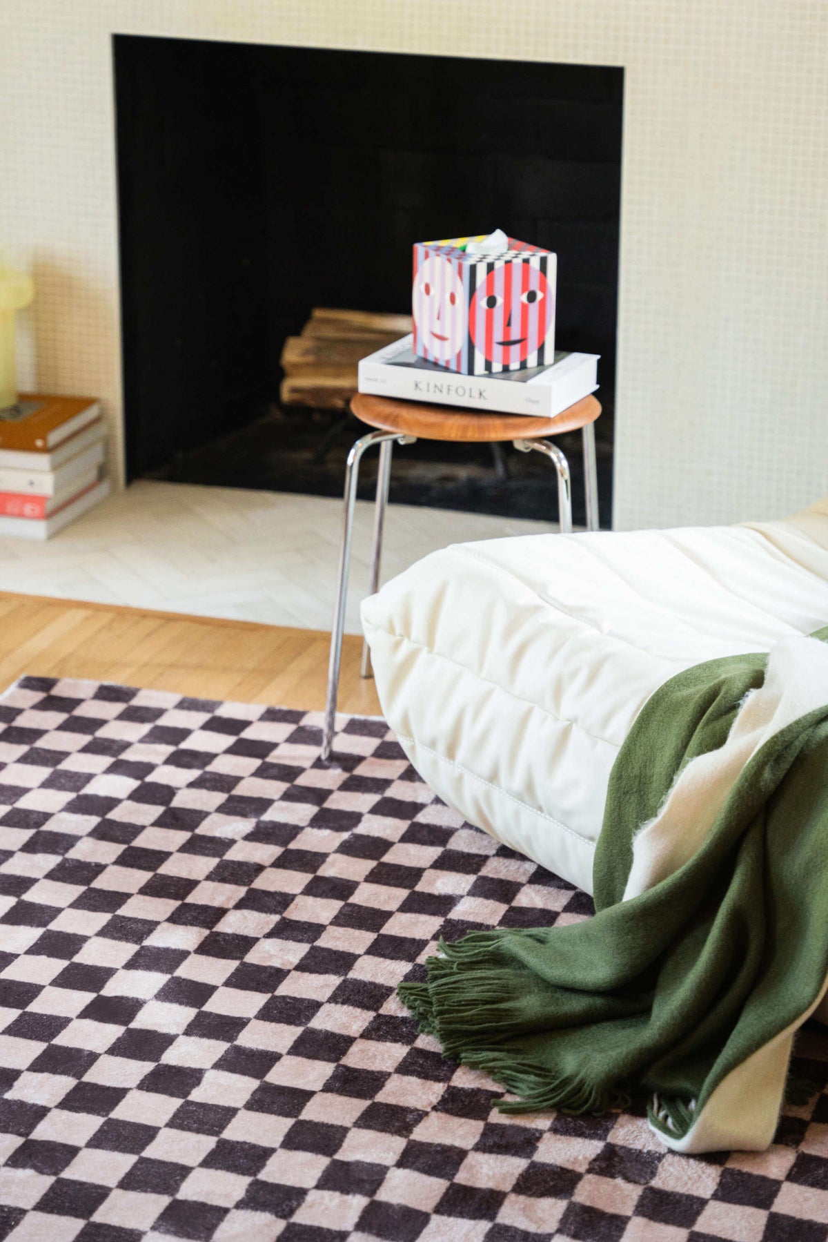 A partial view of the checkered rug by a fireplace, paired with a white chair and green throw for a relaxed corner setup.