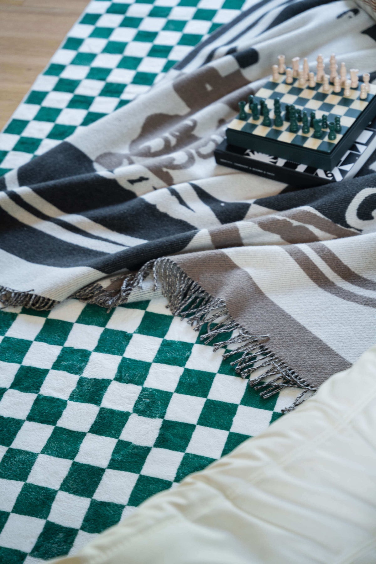Close-up of vibrant checkered rug partially covered with a fringed blanket and a matching green-and-cream chessboard set.
