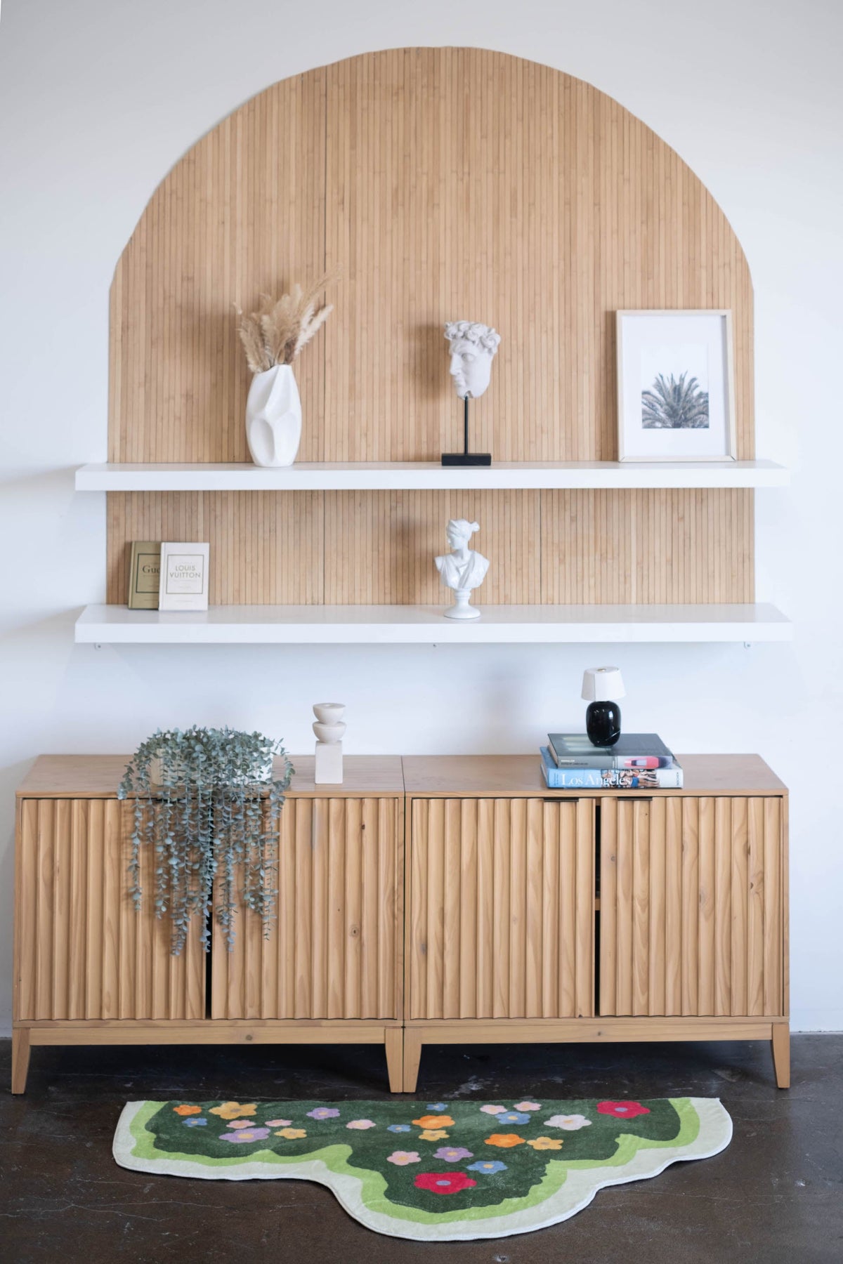 Floral rug styled beneath a wooden console with decorative items and white shelving on the wall.