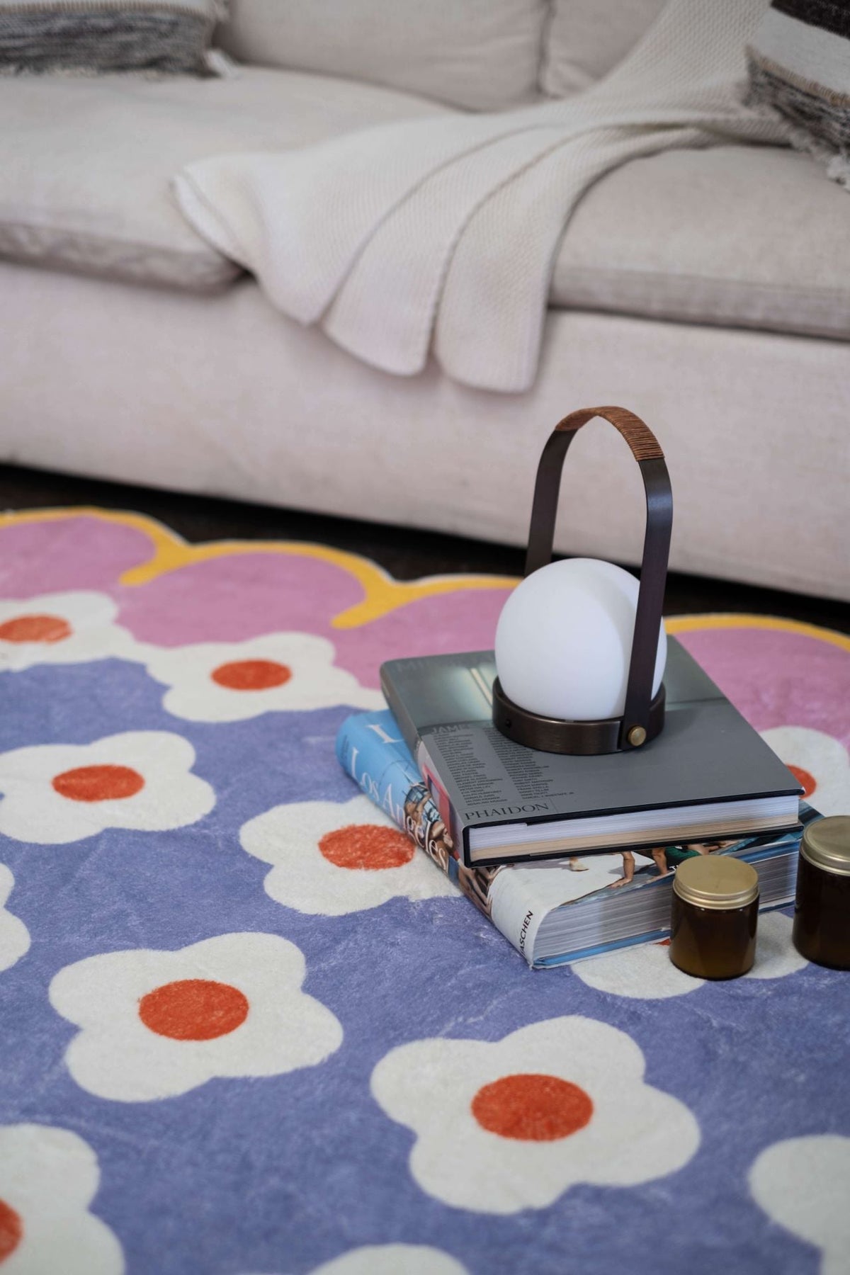 Close-up of the floral area rug’s purple and white flower pattern with books and a modern lamp.