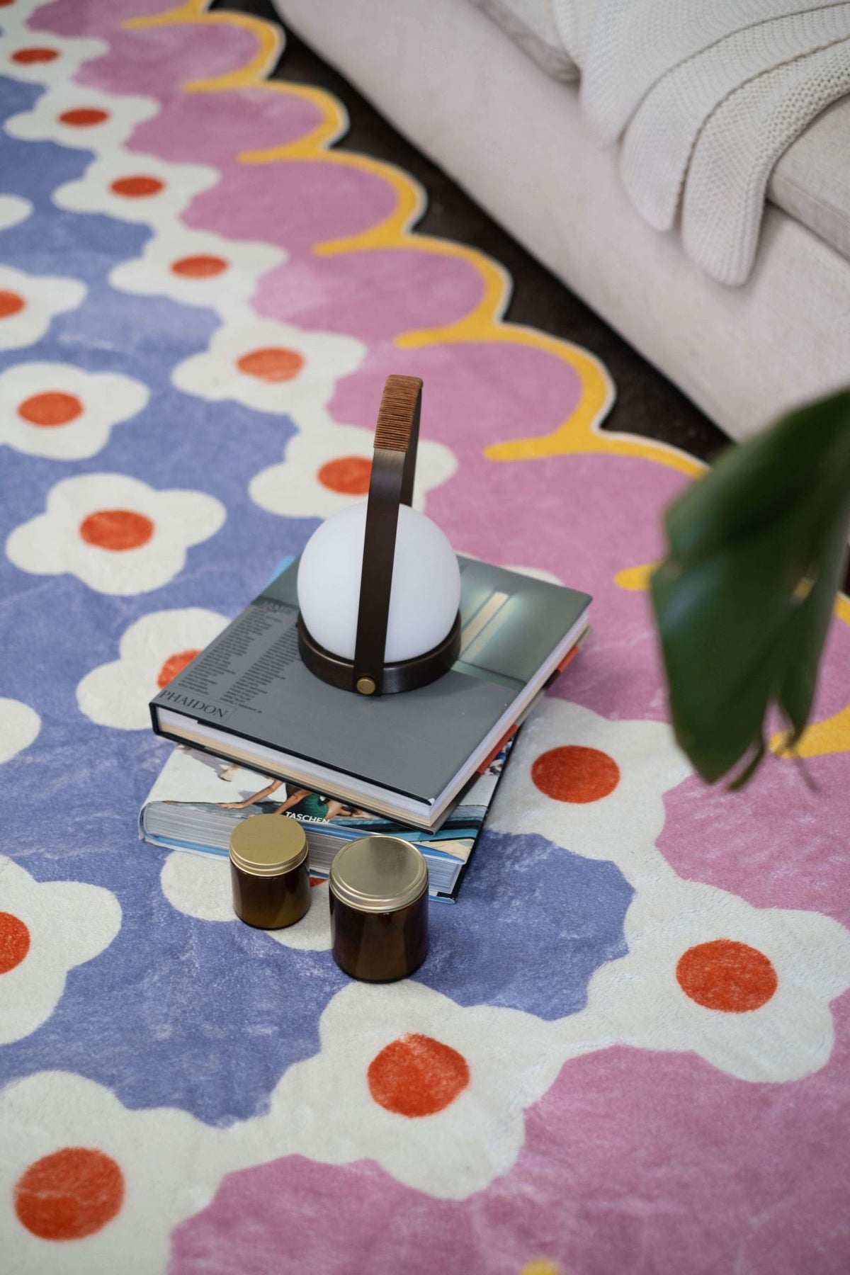 Close-up of the pink and purple floral rug with a lantern lamp and stacked books placed on top.