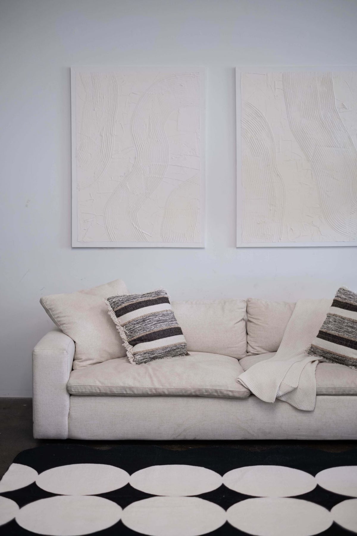 A closer look at the geometric area rug in front of a cream sofa, revealing its bold ivory circle pattern on a black base.