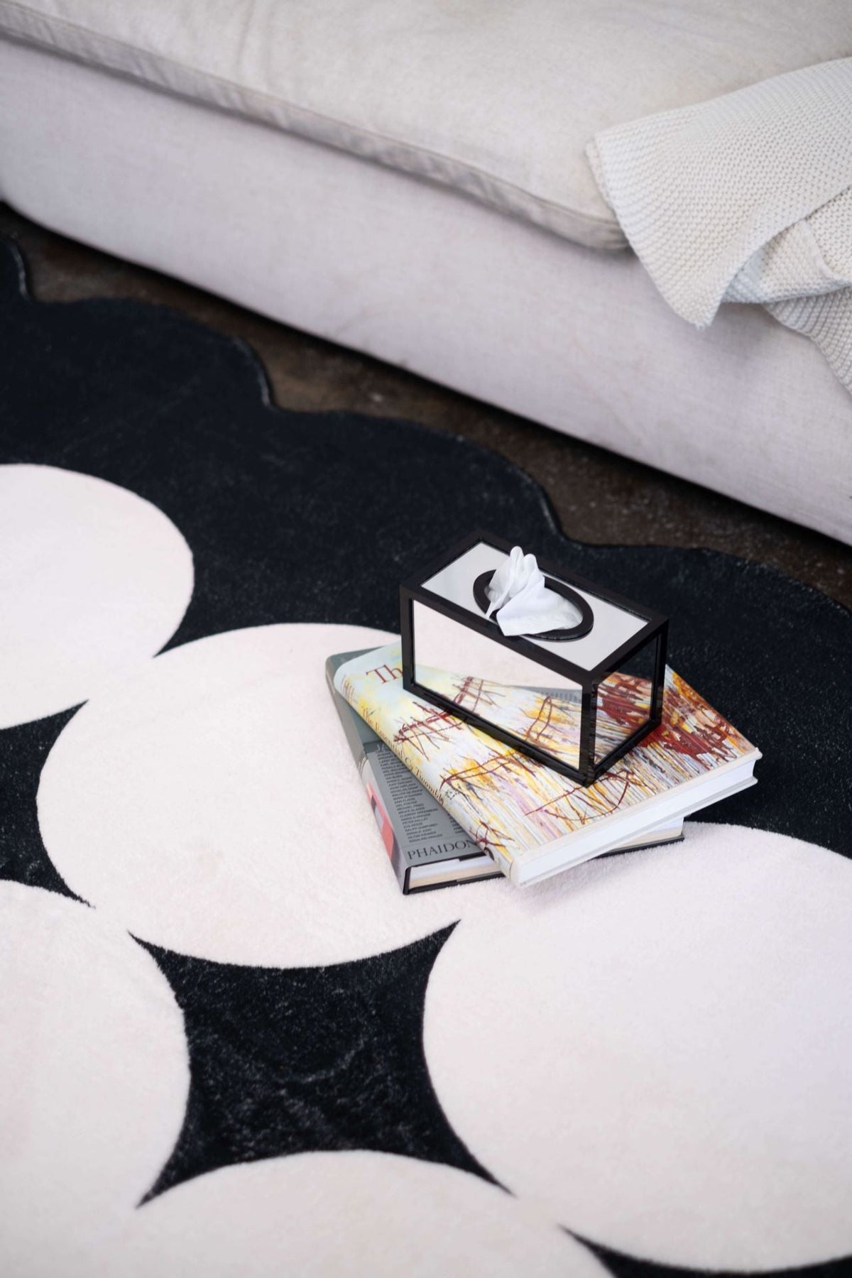 Detail of the geometric rug's edge and pattern with a small stack of books and a mirrored tissue box atop the rug.
