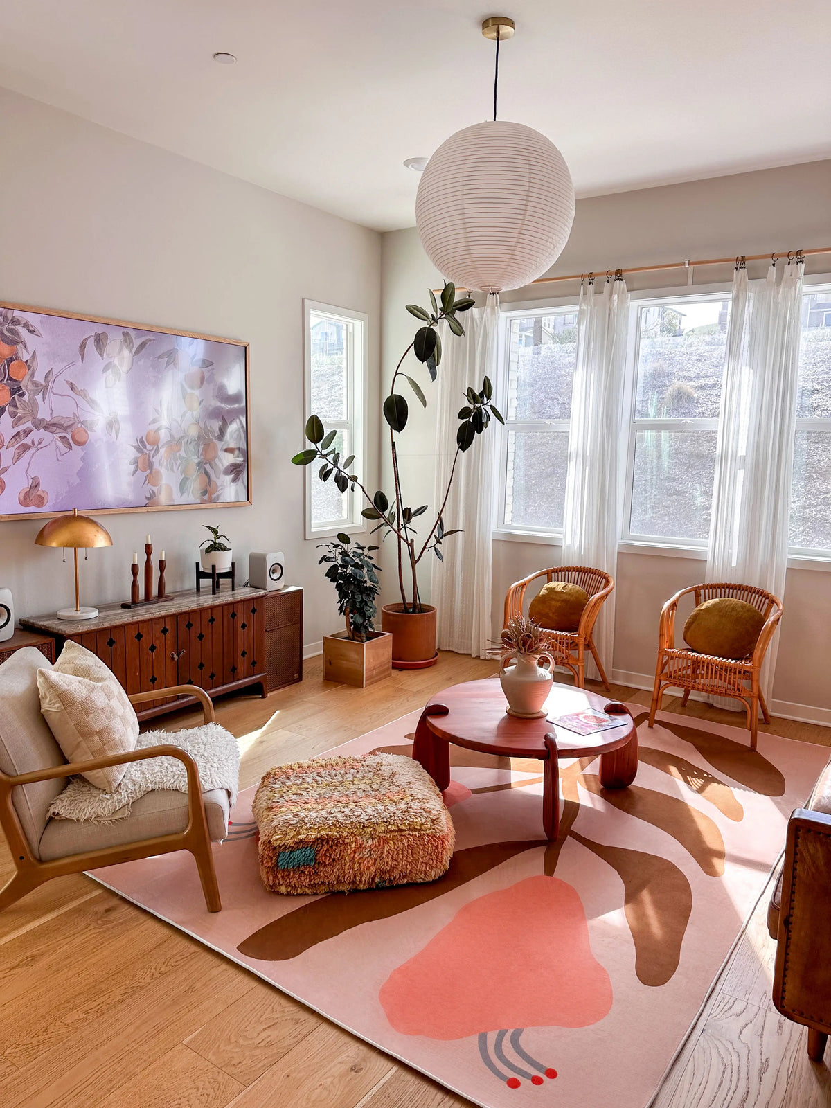 Vintage flower area rug in a bright modern living room with a round wood coffee table, lounge chairs, and pink wall art